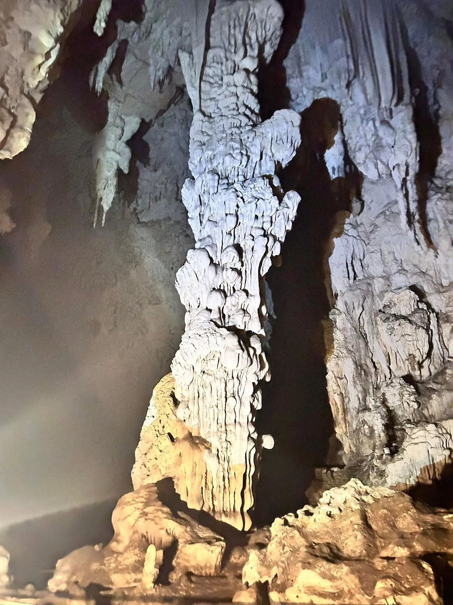 A tall stalagmite lit from below inside a limestone cave