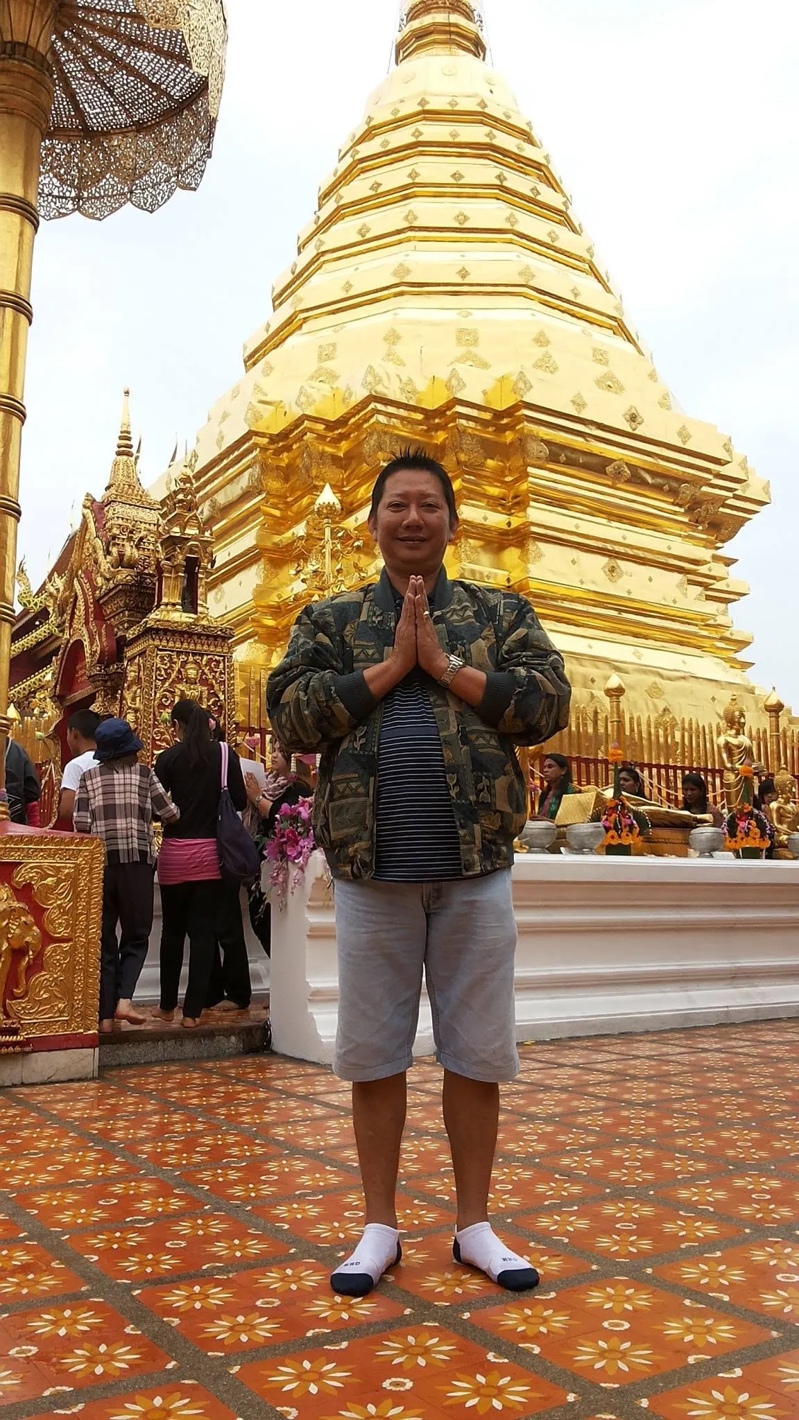 Boon greeting the camera with a wai in front of the golden chedi of Wat Phra That Doi Suthep